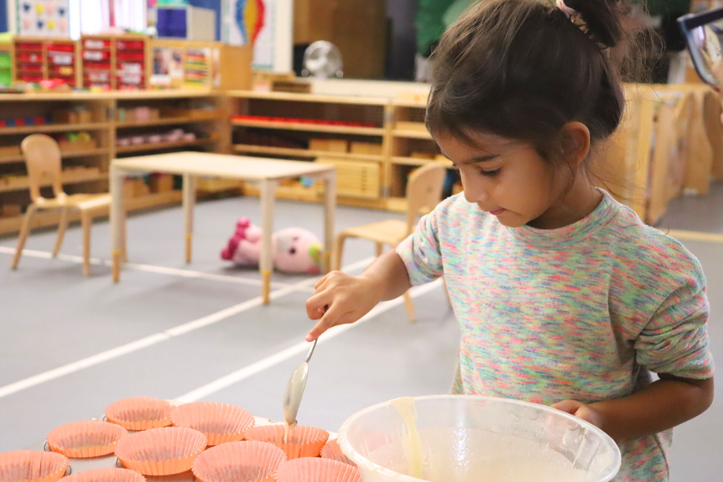 A budding learner scooping cupcake batter into the baking sheet